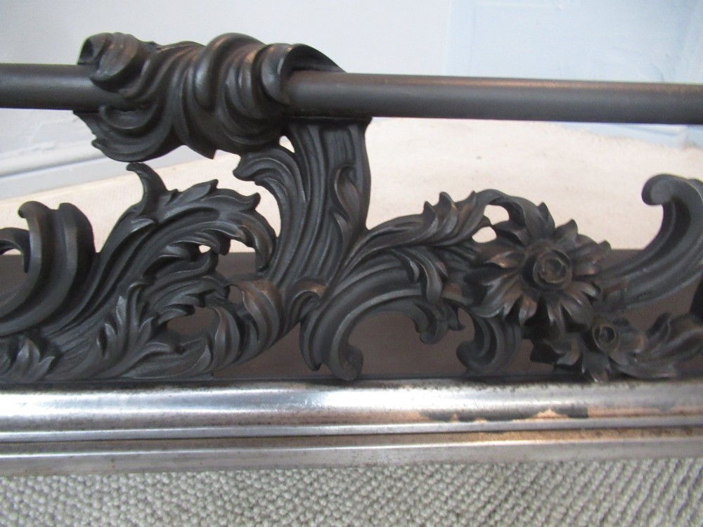 A nineteenth-century cast iron fire fender featuring detailed scrolling foliage ornament, a central spear-head rail, and brass feet. View V