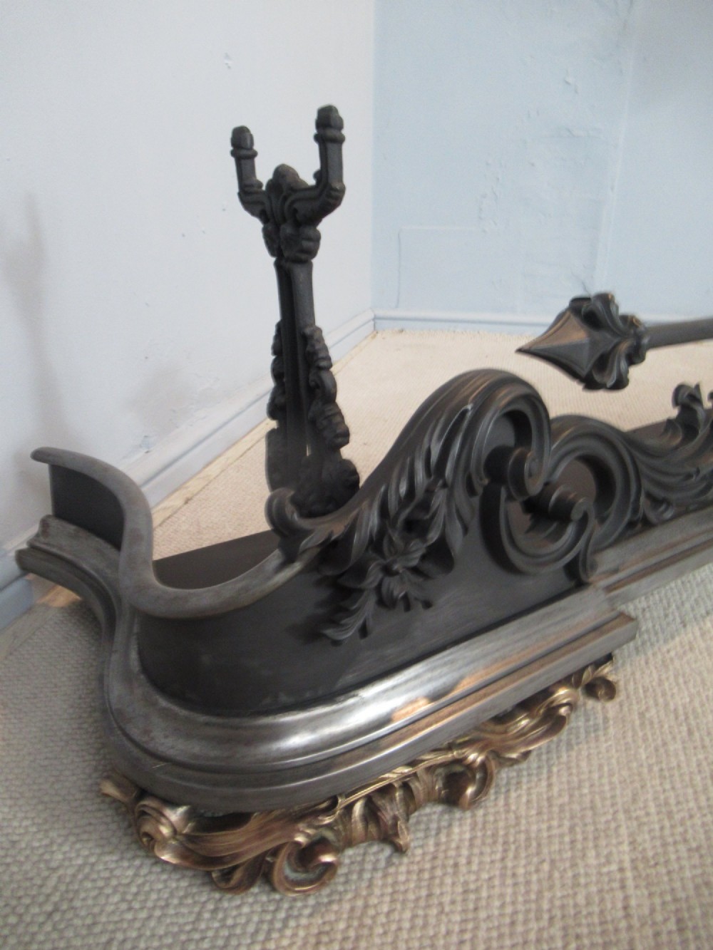 A nineteenth-century cast iron fire fender featuring detailed scrolling foliage ornament, a central spear-head rail, and brass feet. View VIII