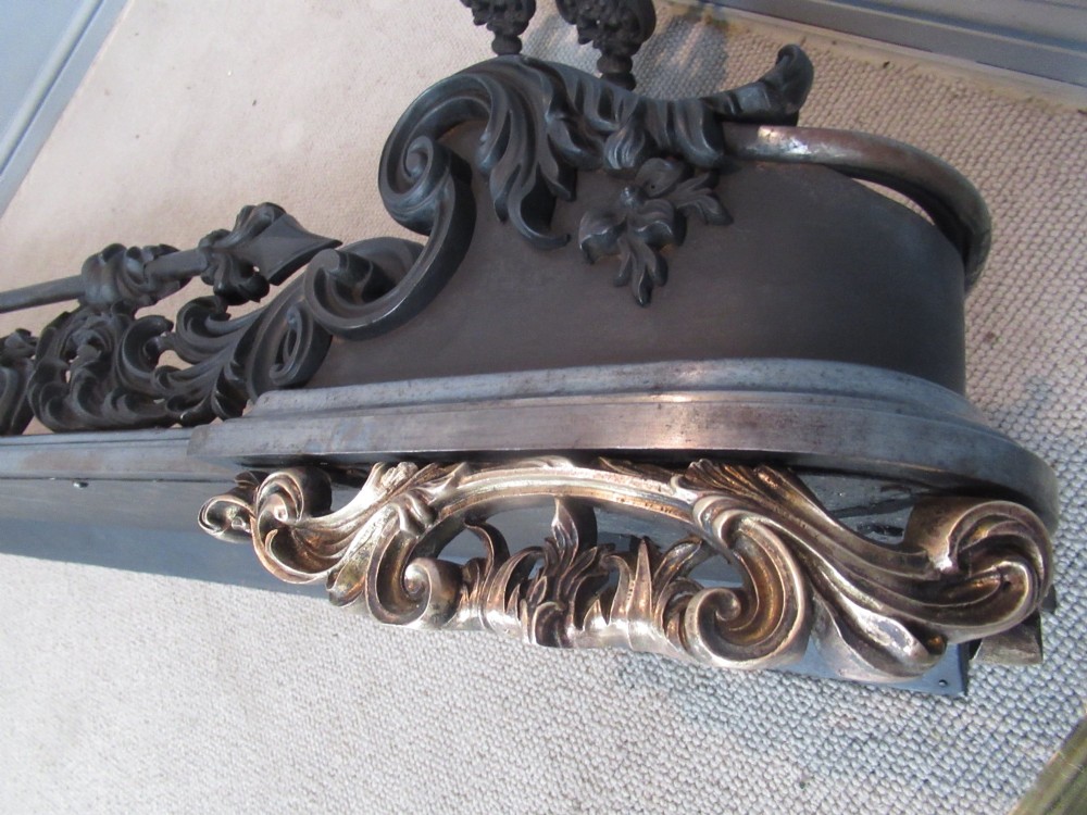 A nineteenth-century cast iron fire fender featuring detailed scrolling foliage ornament, a central spear-head rail, and brass feet. View IX