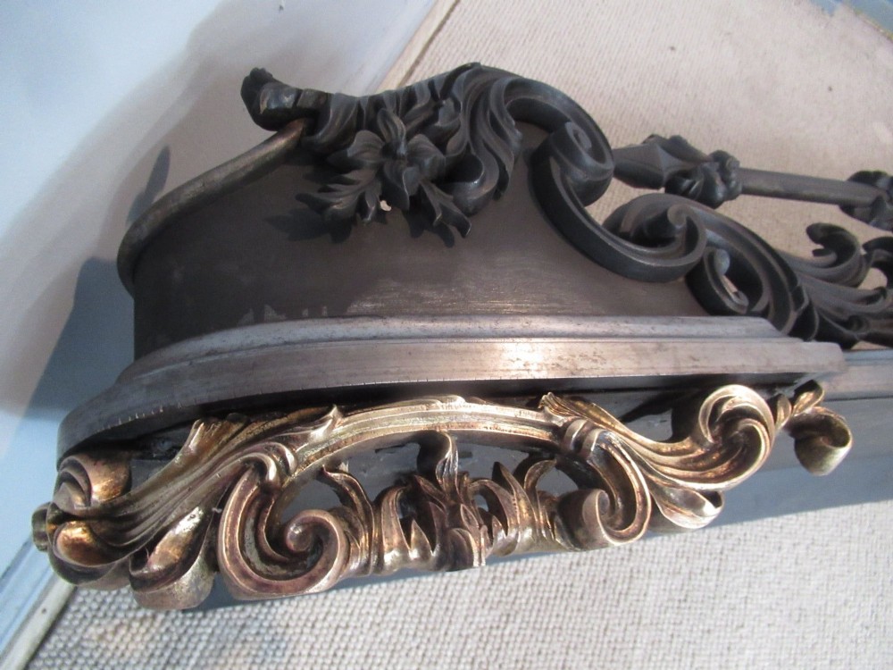 A nineteenth-century cast iron fire fender featuring detailed scrolling foliage ornament, a central spear-head rail, and brass feet. View XI