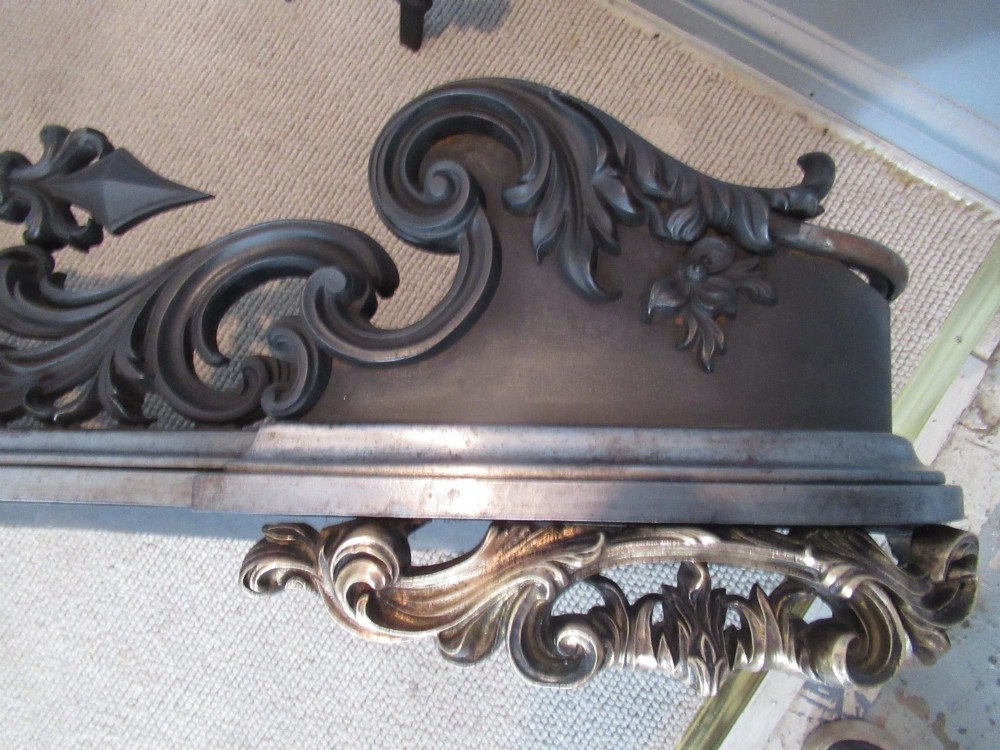 A nineteenth-century cast iron fire fender featuring detailed scrolling foliage ornament, a central spear-head rail, and brass feet. View X