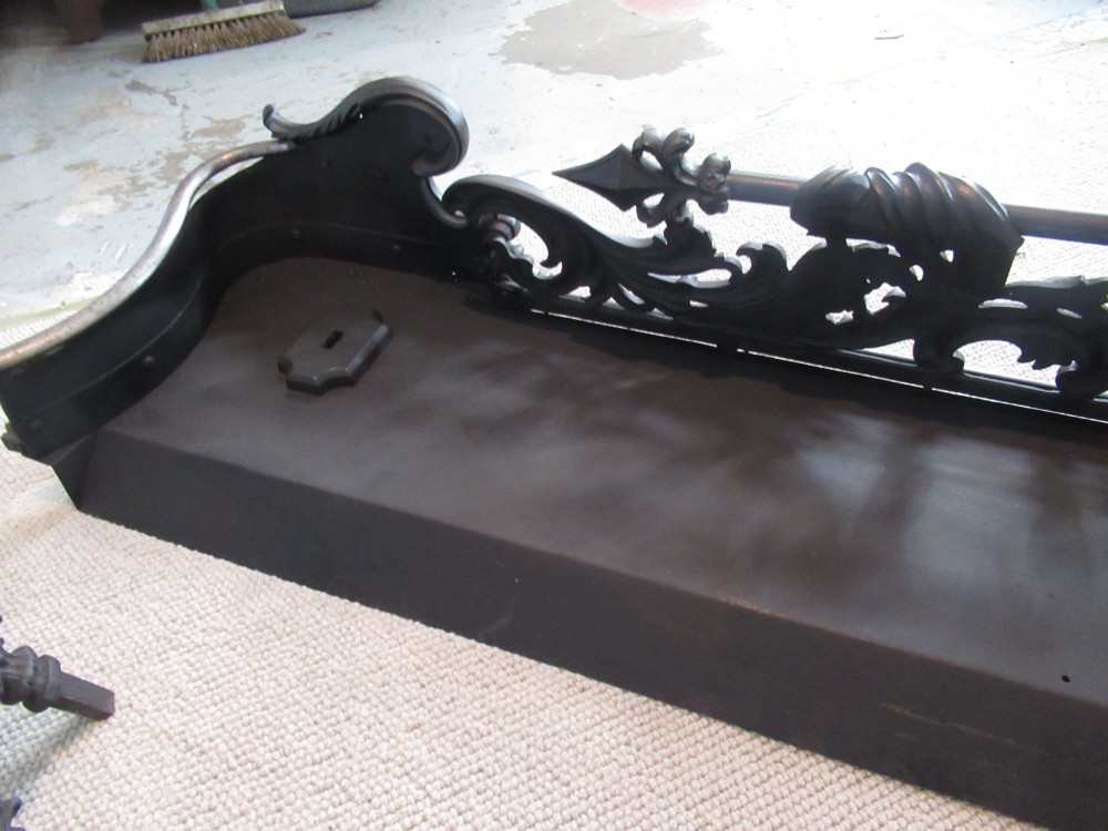 A nineteenth-century cast iron fire fender featuring detailed scrolling foliage ornament, a central spear-head rail, and brass feet. View XII