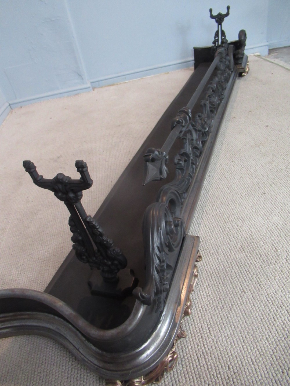 A nineteenth-century cast iron fire fender featuring detailed scrolling foliage ornament, a central spear-head rail, and brass feet. View XIV