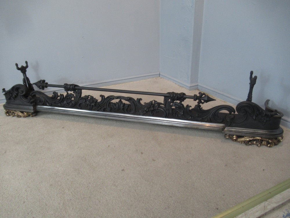 A nineteenth-century cast iron fire fender featuring detailed scrolling foliage ornament, a central spear-head rail, and brass feet. View XV