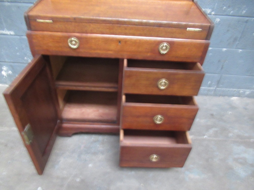 A compact warm brown oak roll top desk featuring a slatted tambour top section, brass ring drawer knobs, a panelled left cupboard, and three stacked side drawers. View V