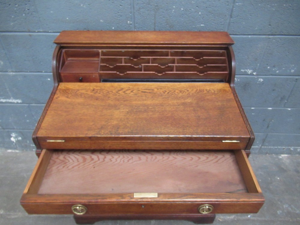 A compact warm brown oak roll top desk featuring a slatted tambour top section, brass ring drawer knobs, a panelled left cupboard, and three stacked side drawers. View VII