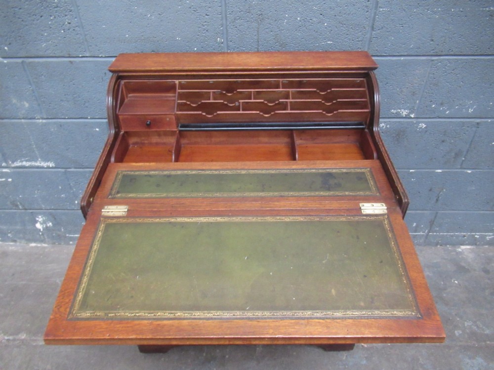 A compact warm brown oak roll top desk featuring a slatted tambour top section, brass ring drawer knobs, a panelled left cupboard, and three stacked side drawers. View VIII
