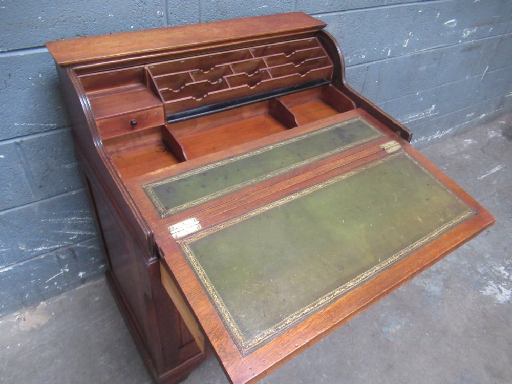 A compact warm brown oak roll top desk featuring a slatted tambour top section, brass ring drawer knobs, a panelled left cupboard, and three stacked side drawers. View IX