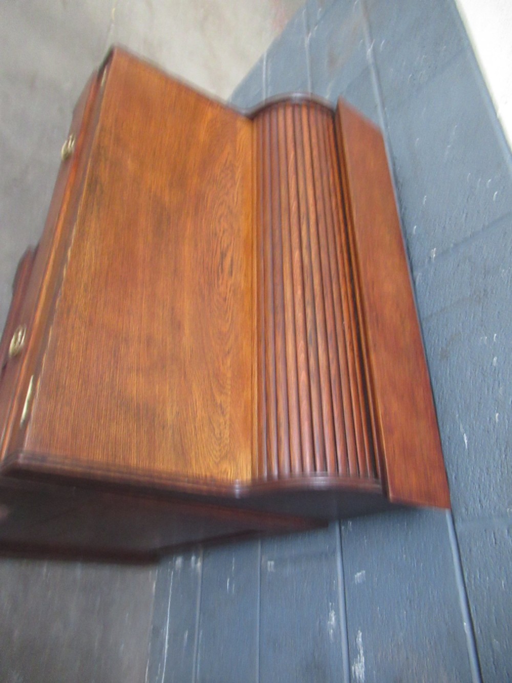 A compact warm brown oak roll top desk featuring a slatted tambour top section, brass ring drawer knobs, a panelled left cupboard, and three stacked side drawers. View XII