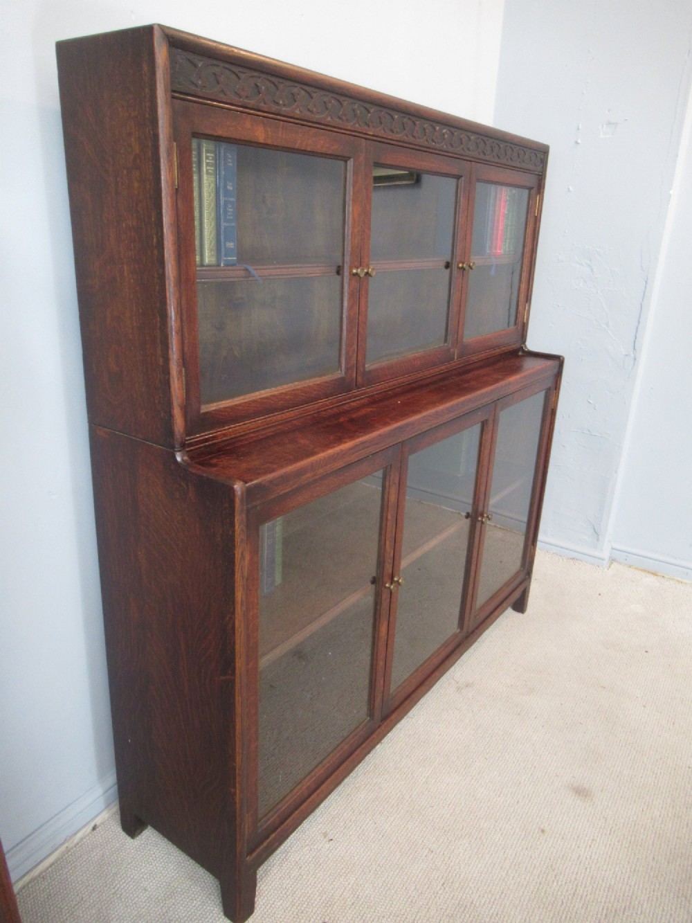 A dark oak two-tiered bookcase featuring six glazed doors, framed glass panels, and a carved top frieze. View III