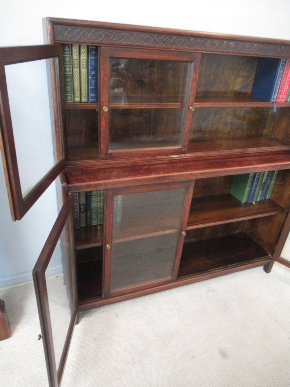 A dark oak two-tiered bookcase featuring six glazed doors, framed glass panels, and a carved top frieze. View V