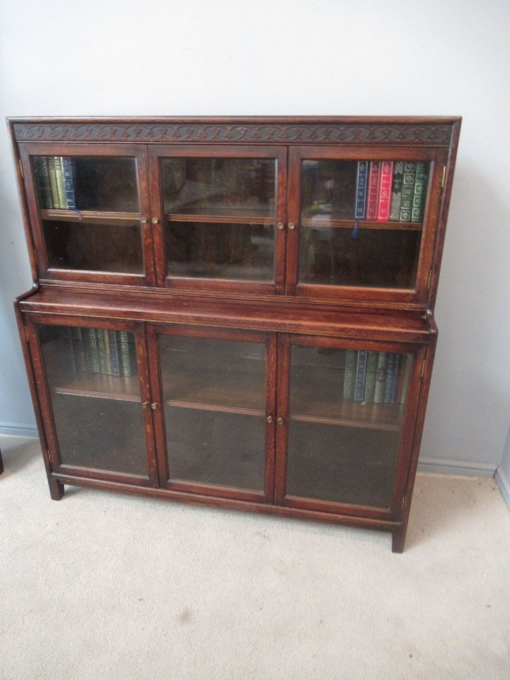 A dark oak two-tiered bookcase featuring six glazed doors, framed glass panels, and a carved top frieze. View X