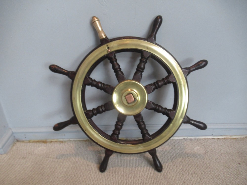A 19th-century turned dark hardwood ships wheel featuring eight handles, a central brass nave plate, and a brass outer brass band.