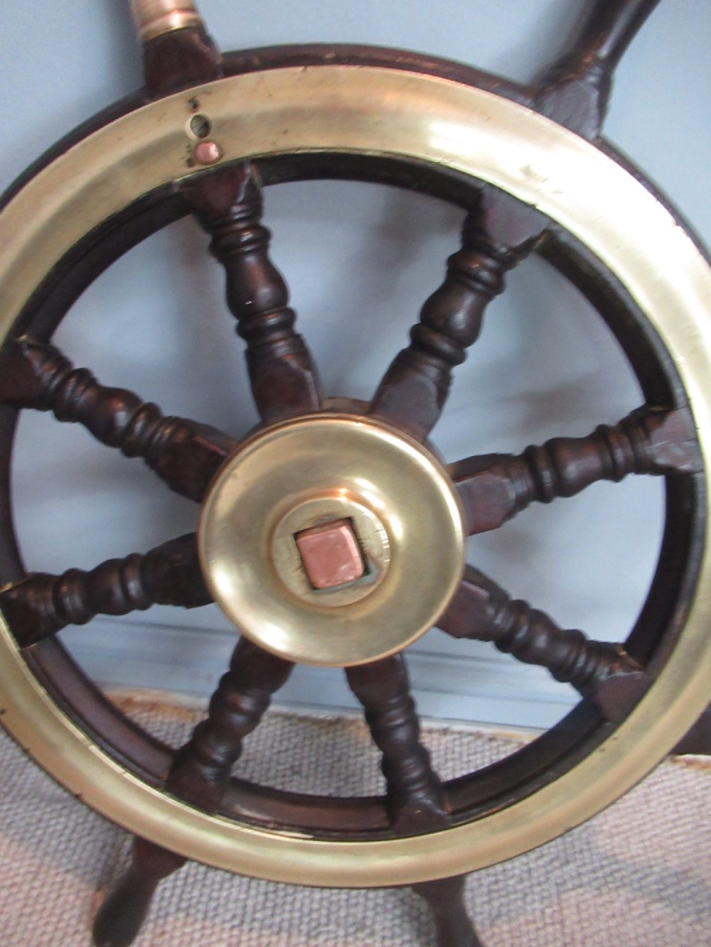 A 19th-century turned dark hardwood ships wheel featuring eight handles, a central brass nave plate, and a brass outer brass band. View VI