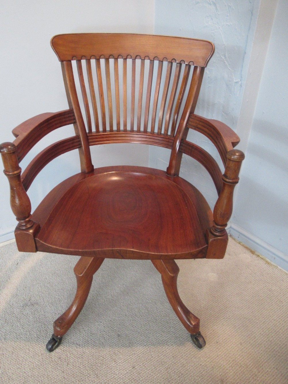 A Victorian walnut swivel office chair with a curved spindle backrest, contoured saddle seat, and quadruped base on castors.