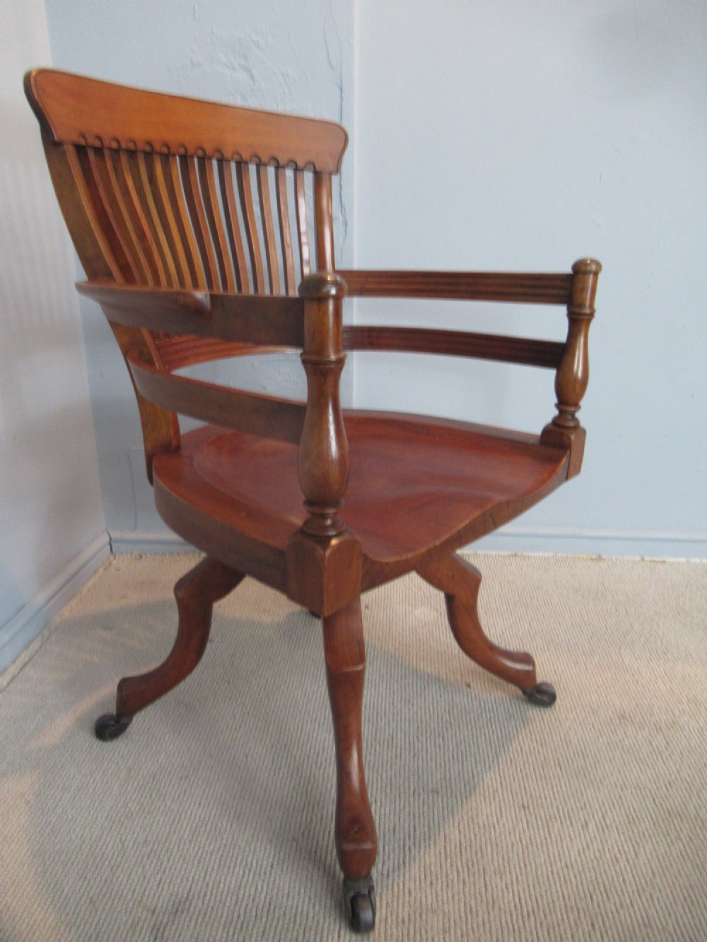 A Victorian walnut swivel office chair with a curved spindle backrest, contoured saddle seat, and quadruped base on castors. View II