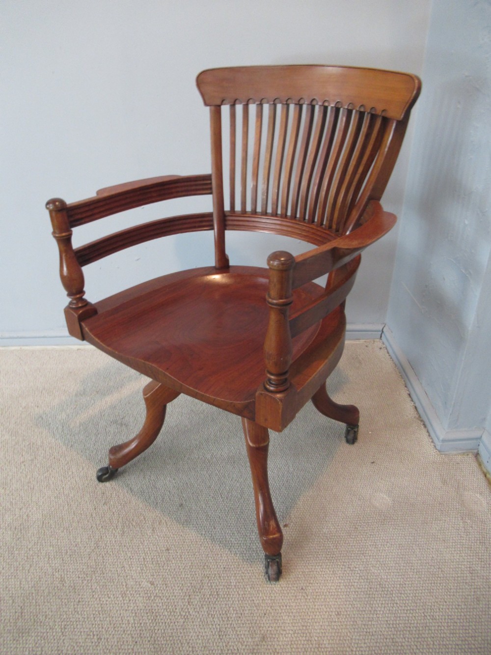 A Victorian walnut swivel office chair with a curved spindle backrest, contoured saddle seat, and quadruped base on castors. View III