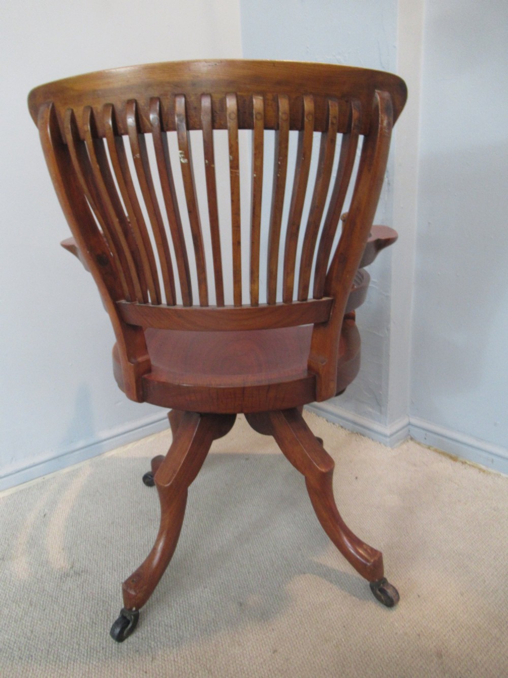 A Victorian walnut swivel office chair with a curved spindle backrest, contoured saddle seat, and quadruped base on castors. View IV