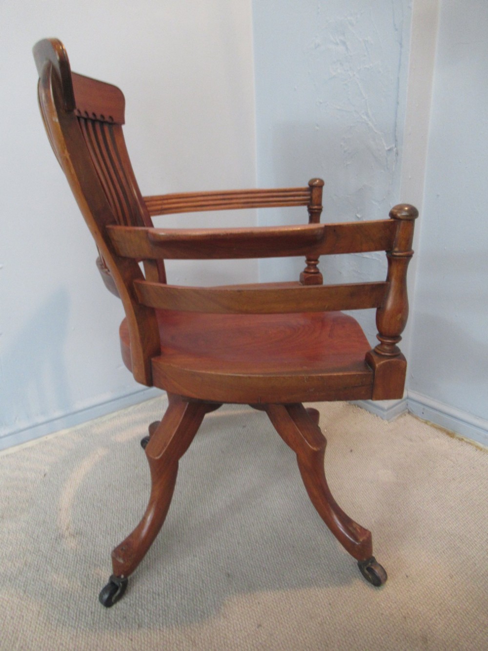 A Victorian walnut swivel office chair with a curved spindle backrest, contoured saddle seat, and quadruped base on castors. View IX