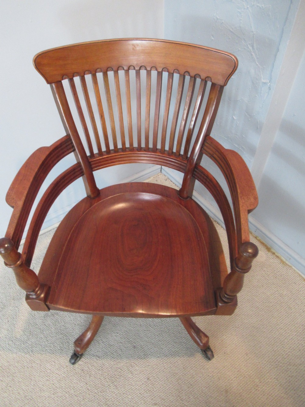 A Victorian walnut swivel office chair with a curved spindle backrest, contoured saddle seat, and quadruped base on castors. View X