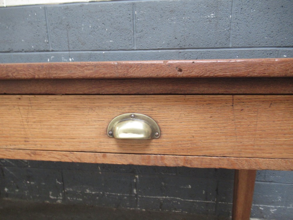 A light oak side table featuring a wide rectangular top, two drawers with brass cup handles, and four straight legs. View VI