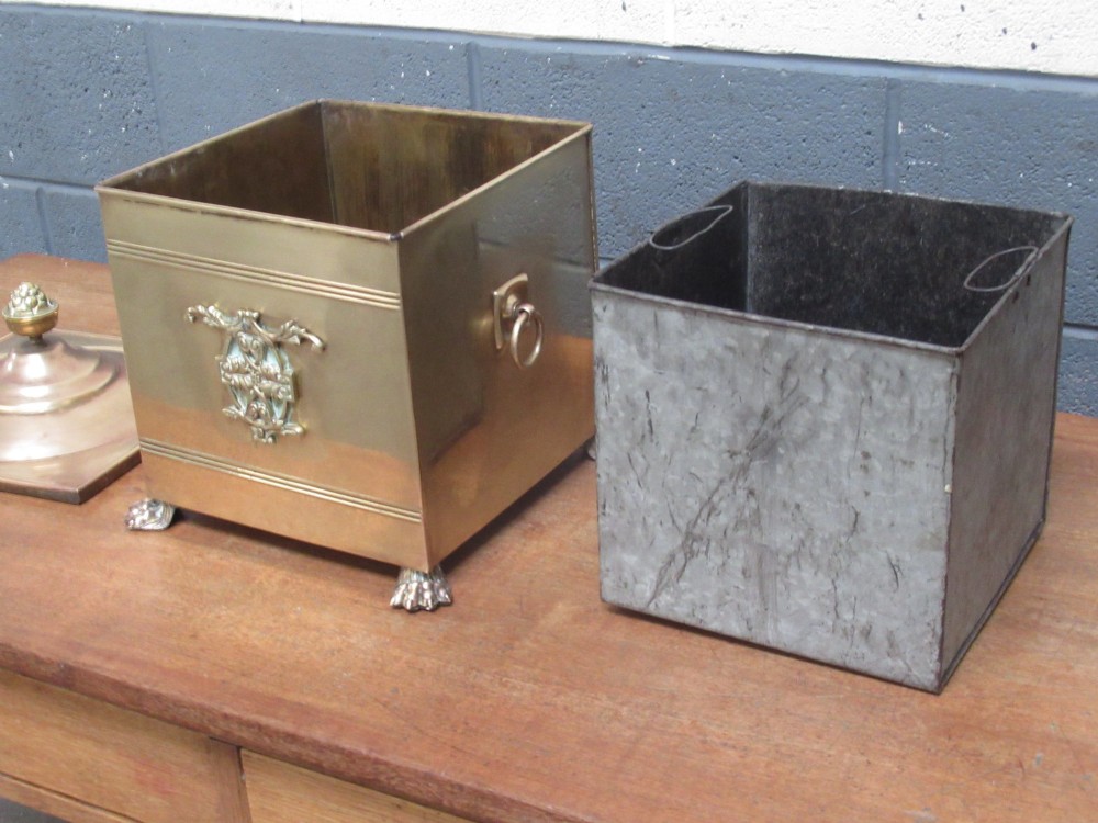 A square brass coal bin featuring a domed copper-toned lid topped with a finial, side drop ring handles, a relief crest, and claw feet. View VII