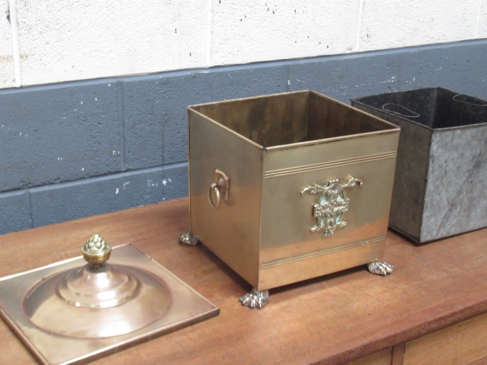 A square brass coal bin featuring a domed copper-toned lid topped with a finial, side drop ring handles, a relief crest, and claw feet. View VIII