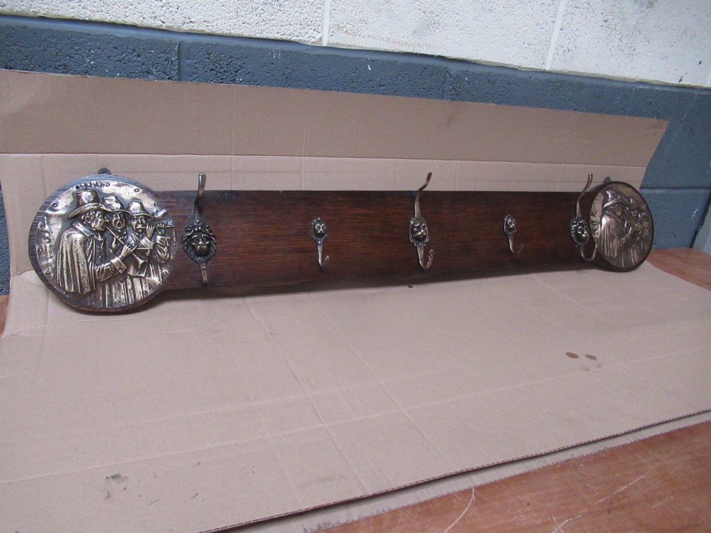 A horizontal dark oak wall-mounted coat rack featuring metal coat hooks and round relief panels depicting figures. View II