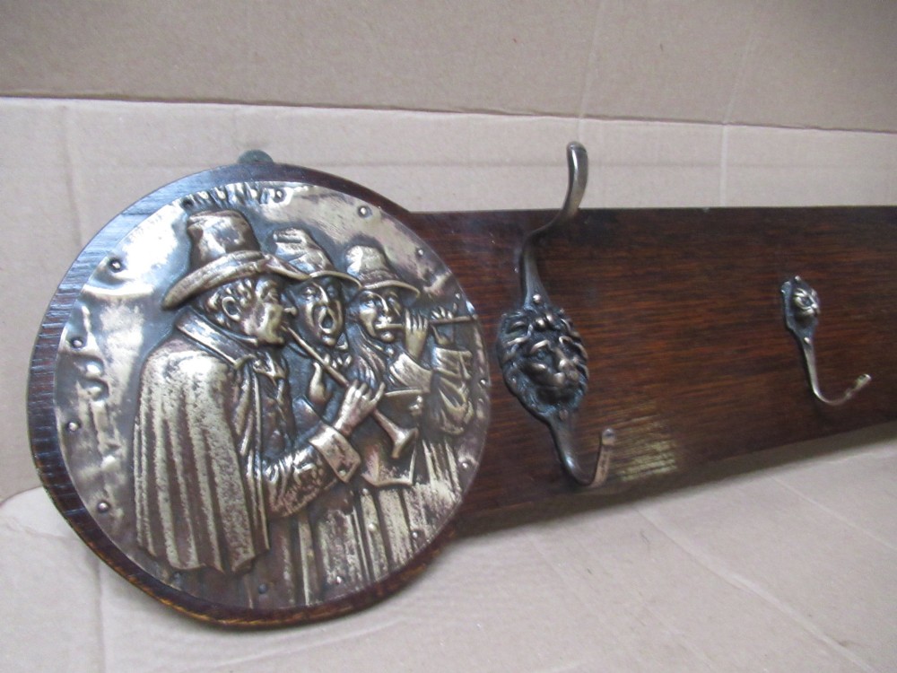 A horizontal dark oak wall-mounted coat rack featuring metal coat hooks and round relief panels depicting figures. View IV