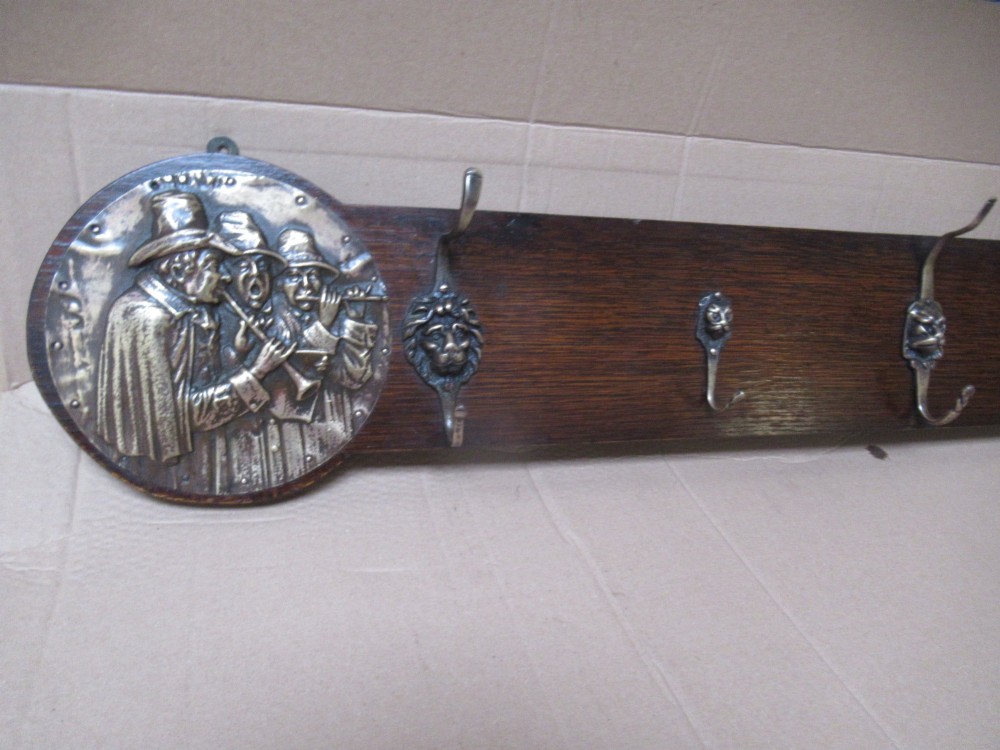 A horizontal dark oak wall-mounted coat rack featuring metal coat hooks and round relief panels depicting figures. View VI