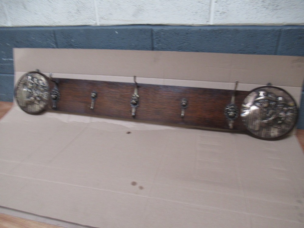 A horizontal dark oak wall-mounted coat rack featuring metal coat hooks and round relief panels depicting figures. View VII