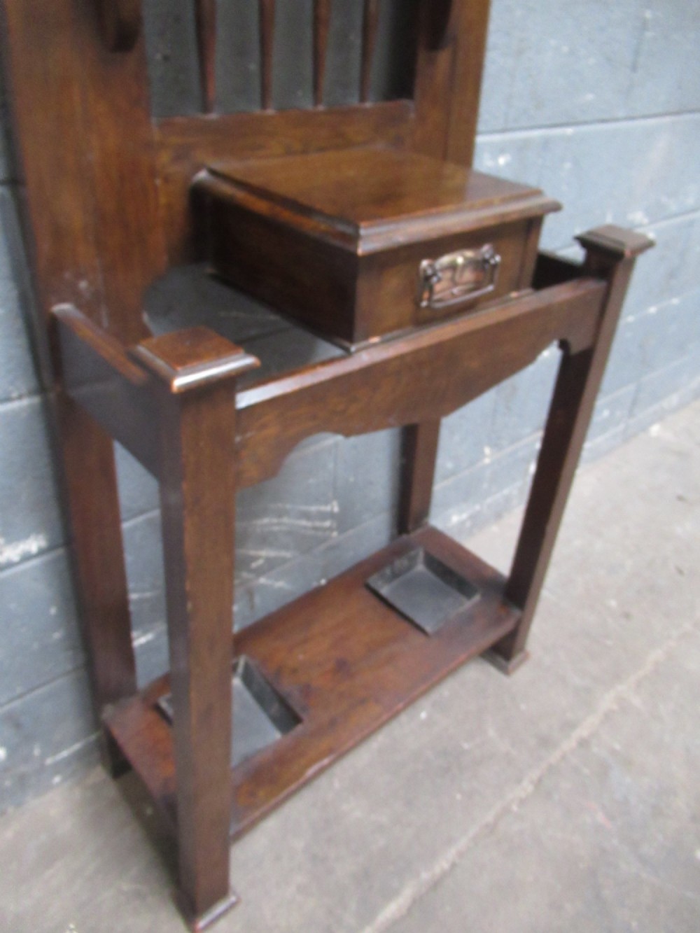 A tall dark oak hall stand featuring an upper arched mirror, metal coat hooks, a central glove box drawer, and lower umbrella holders with removable drip trays. View III