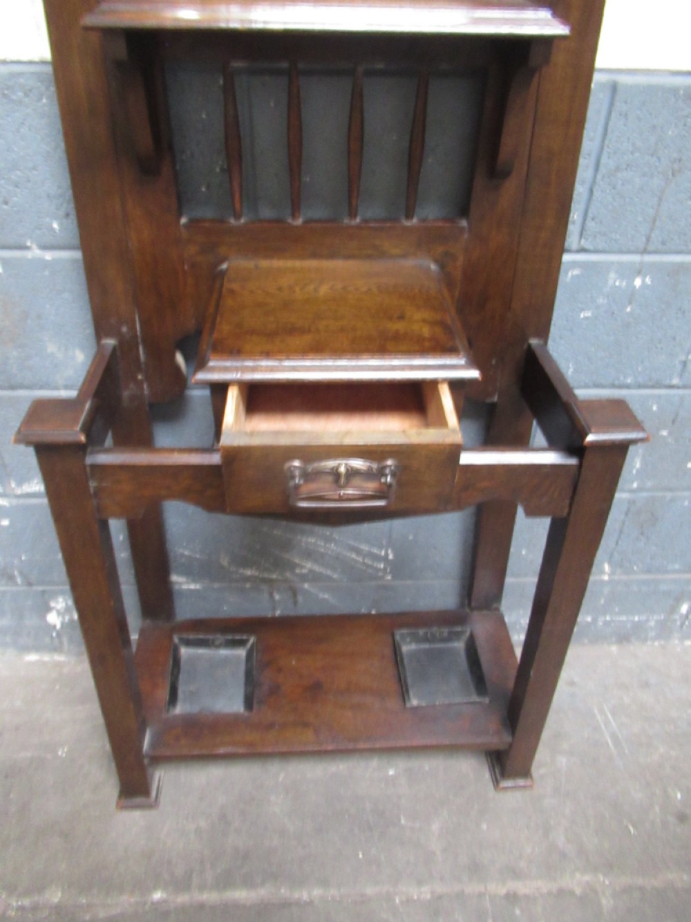 A tall dark oak hall stand featuring an upper arched mirror, metal coat hooks, a central glove box drawer, and lower umbrella holders with removable drip trays. View IV