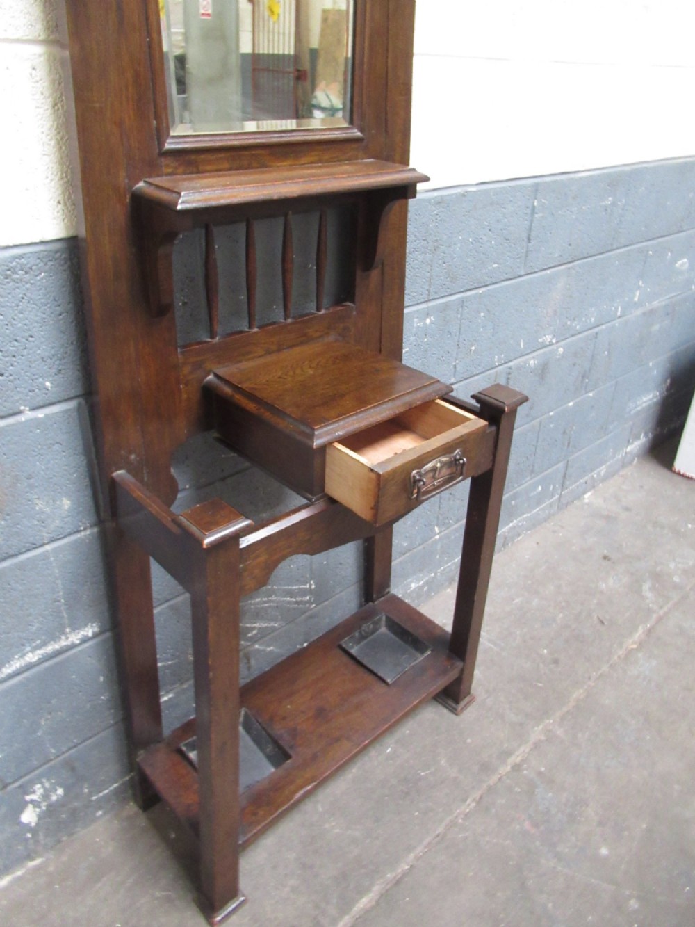 A tall dark oak hall stand featuring an upper arched mirror, metal coat hooks, a central glove box drawer, and lower umbrella holders with removable drip trays. View V