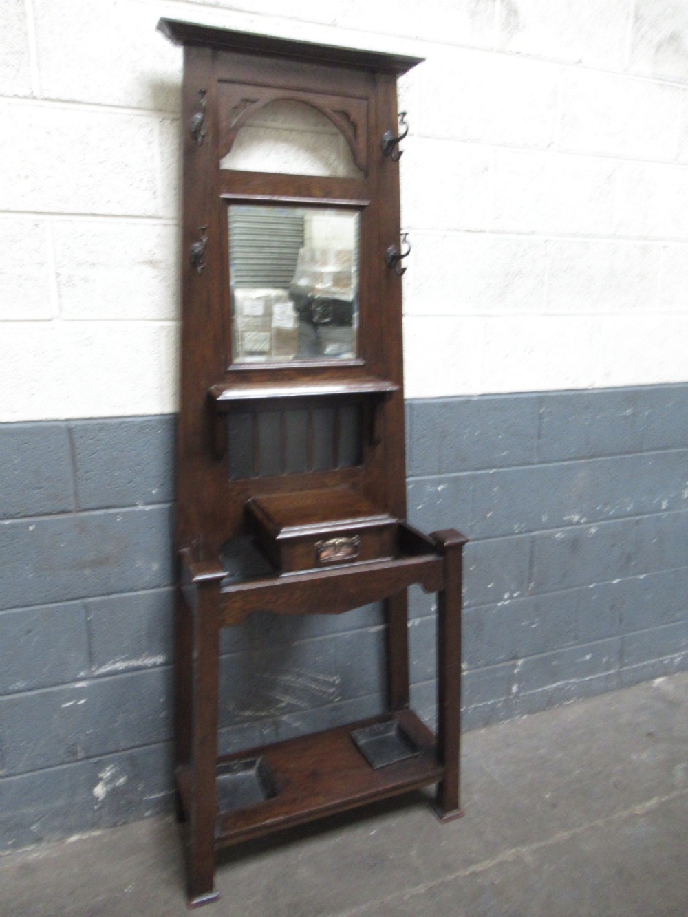 A tall dark oak hall stand featuring an upper arched mirror, metal coat hooks, a central glove box drawer, and lower umbrella holders with removable drip trays. View VIII