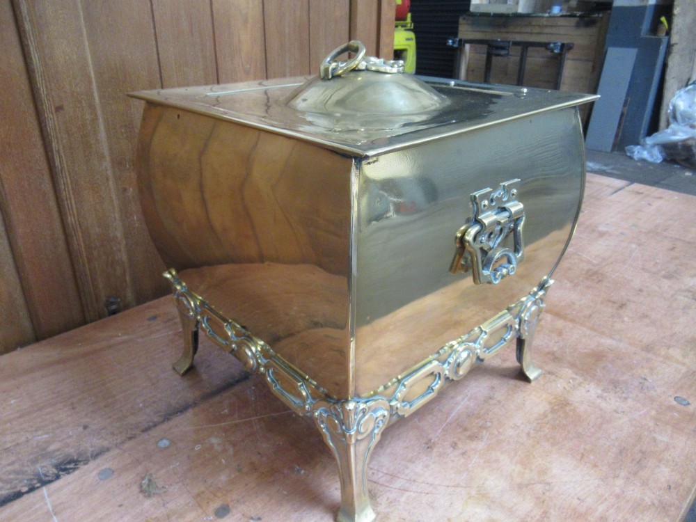 An Edwardian square brass coal box featuring a domed central lid handle, side drop handles, and ornate cast feet.