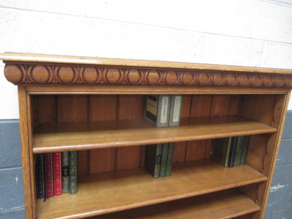 A late Victorian light oak open bookcase featuring five shelves, a planked pine back, and a carved egg-and-dart cornice moulding. View V