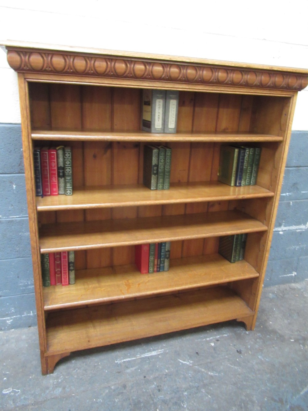A late Victorian light oak open bookcase featuring five shelves, a planked pine back, and a carved egg-and-dart cornice moulding. View IX