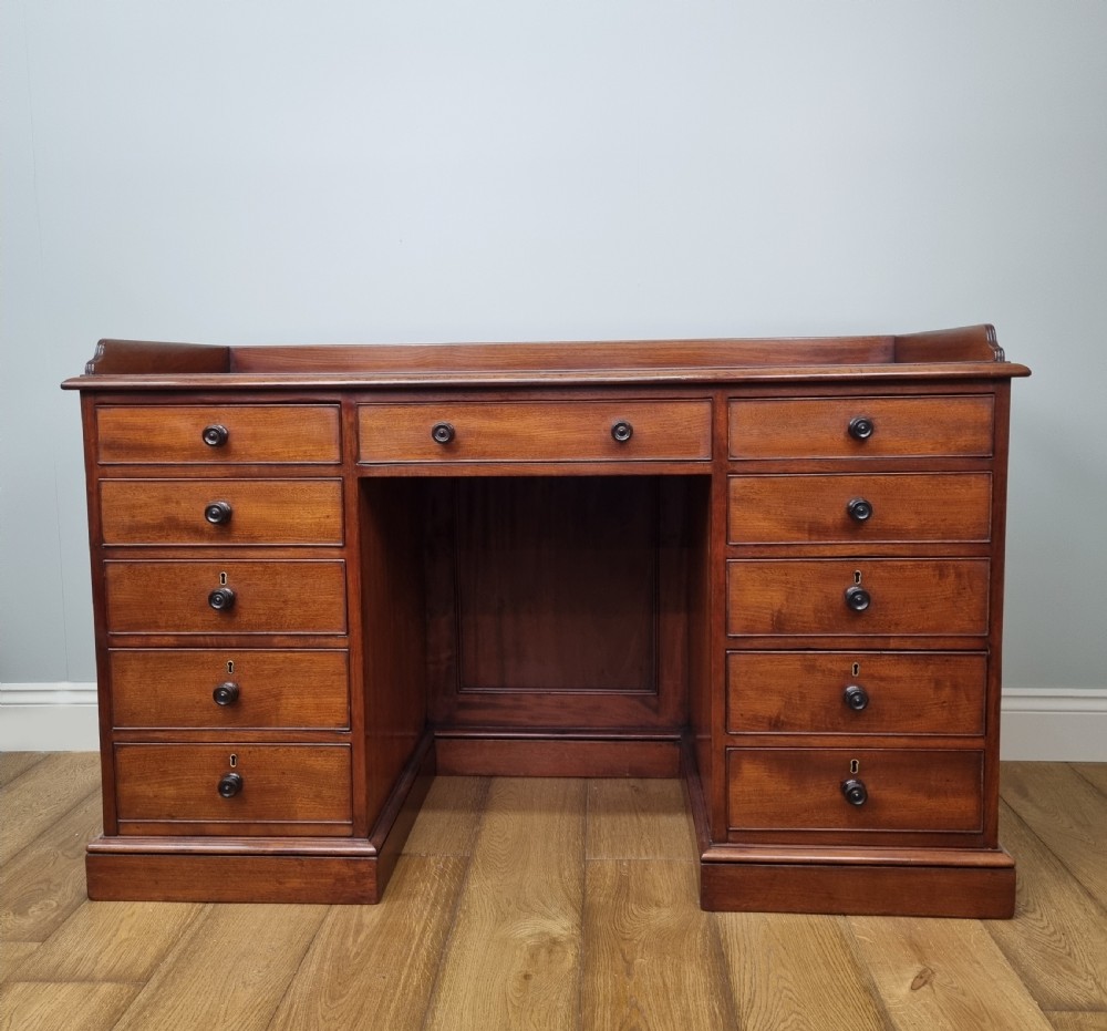An early nineteenth-century mahogany pedestal desk featuring a raised tray top, nine drawers with turned wooden handles, and a central kneehole. View XII