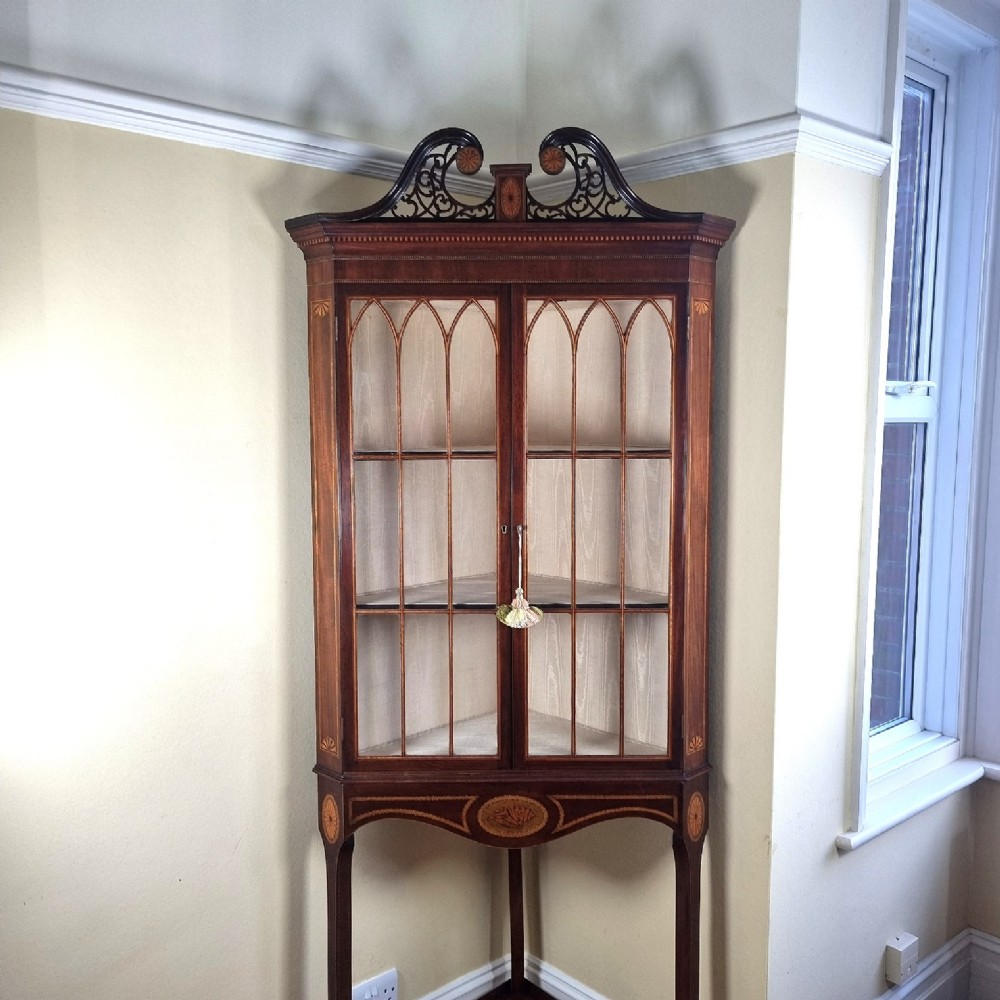 A mahogany Georgian corner display cabinet on stand featuring gothic astragal glazed doors, a swan-neck pediment, marquetry inlays, and curved lower legs. View II