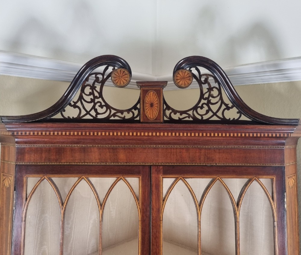 A mahogany Georgian corner display cabinet on stand featuring gothic astragal glazed doors, a swan-neck pediment, marquetry inlays, and curved lower legs. View V