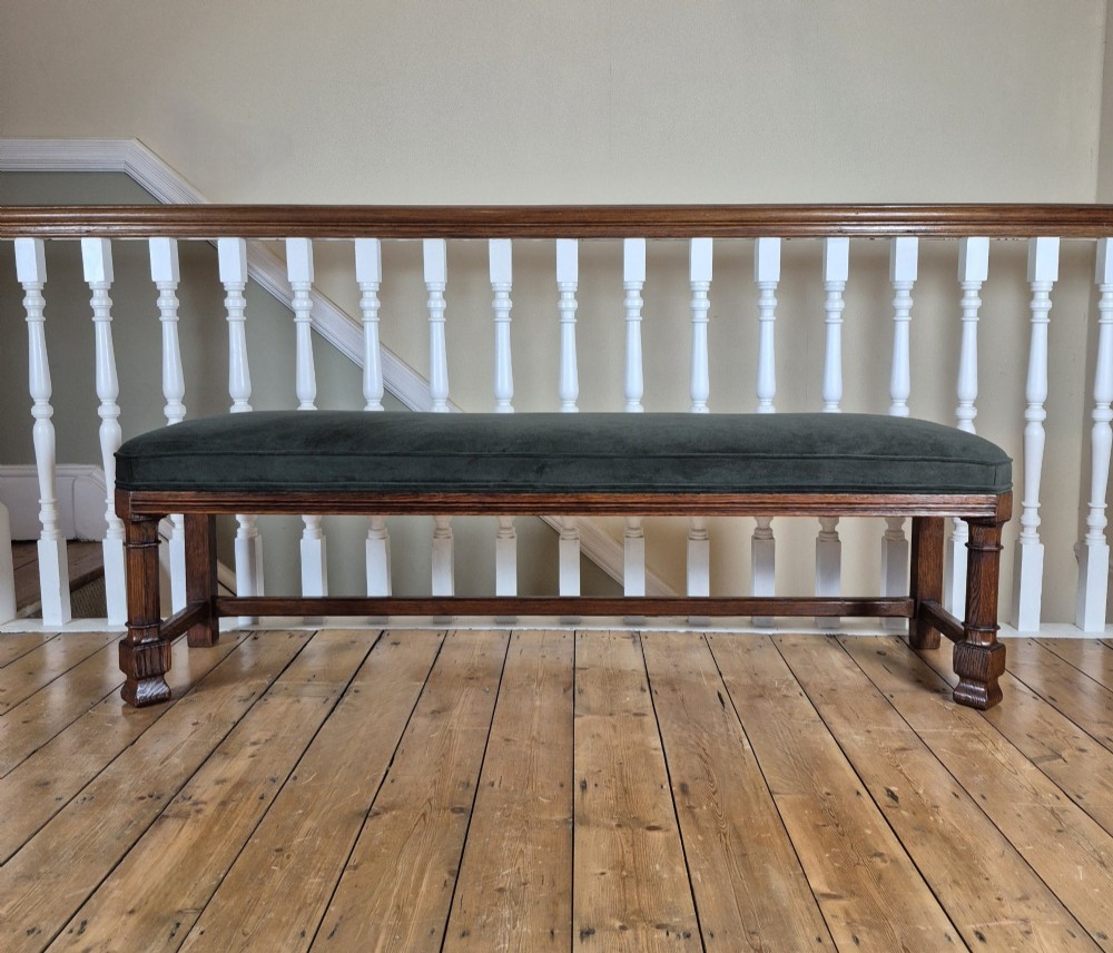 A long Victorian Gothic Revival solid oak bench featuring turned legs, a rectangular lower stretcher frame, and a dark green velvet upholstered cushion top.