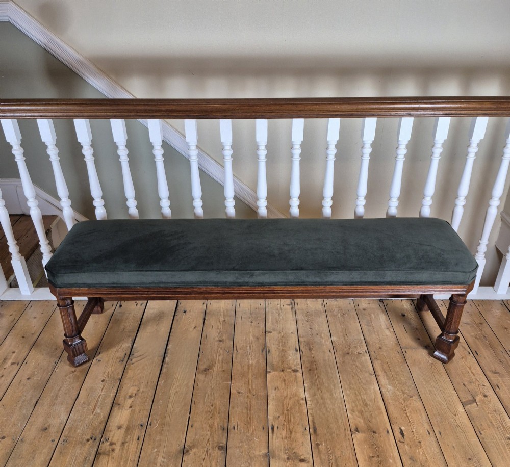 A long Victorian Gothic Revival solid oak bench featuring turned legs, a rectangular lower stretcher frame, and a dark green velvet upholstered cushion top. View II