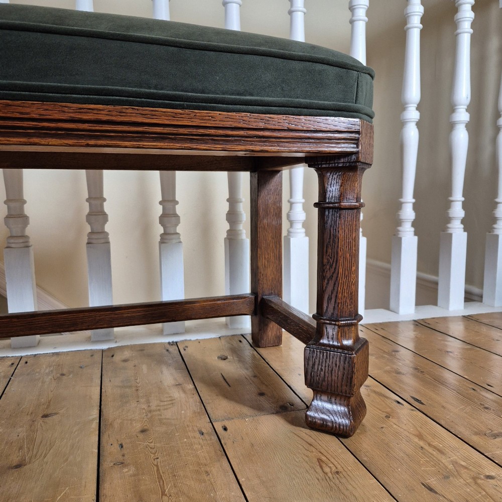 A long Victorian Gothic Revival solid oak bench featuring turned legs, a rectangular lower stretcher frame, and a dark green velvet upholstered cushion top. View III