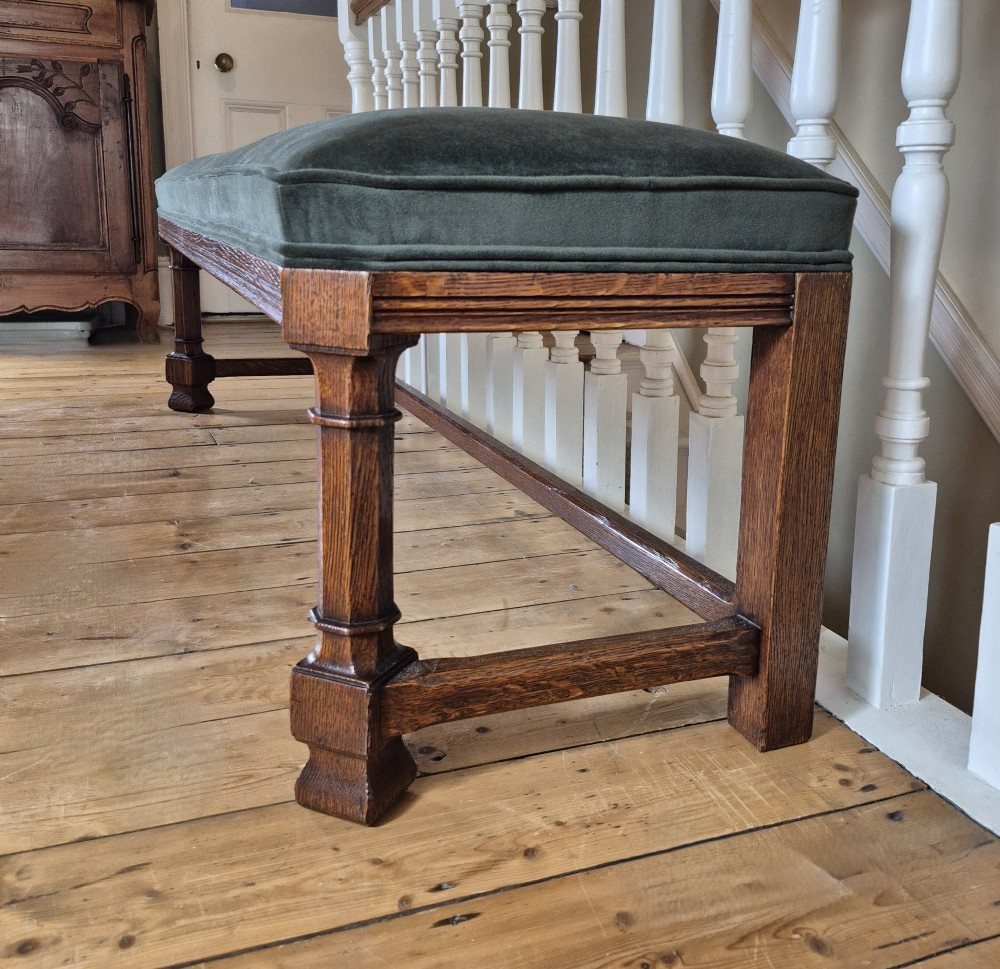 A long Victorian Gothic Revival solid oak bench featuring turned legs, a rectangular lower stretcher frame, and a dark green velvet upholstered cushion top. View IV