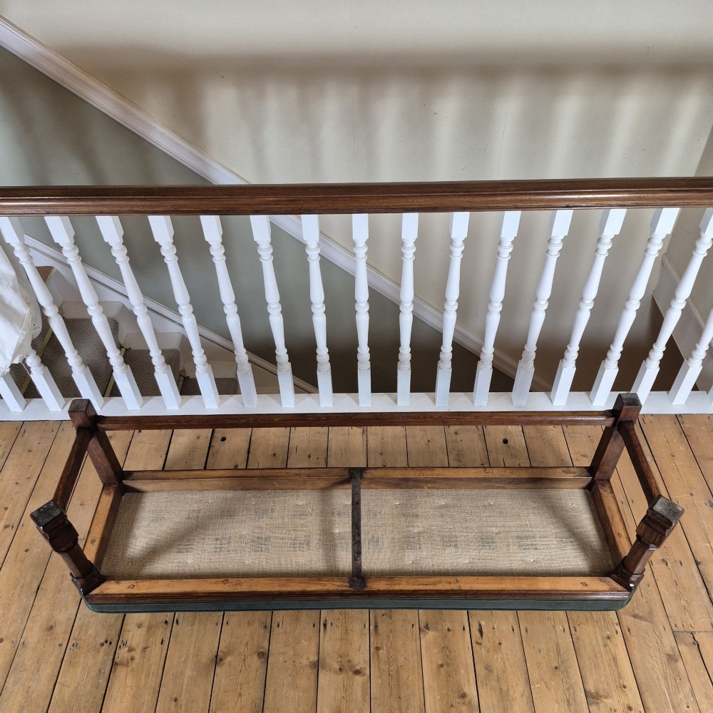 A long Victorian Gothic Revival solid oak bench featuring turned legs, a rectangular lower stretcher frame, and a dark green velvet upholstered cushion top. View VII