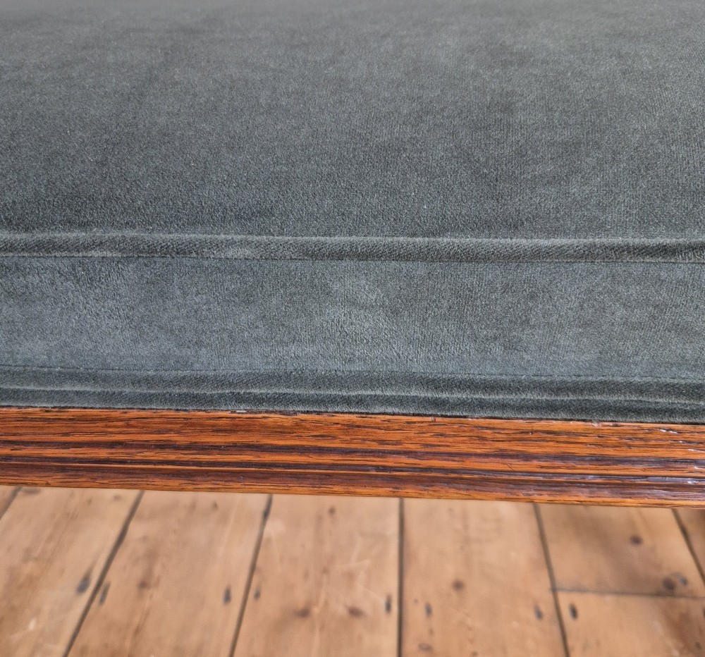 A long Victorian Gothic Revival solid oak bench featuring turned legs, a rectangular lower stretcher frame, and a dark green velvet upholstered cushion top. View X