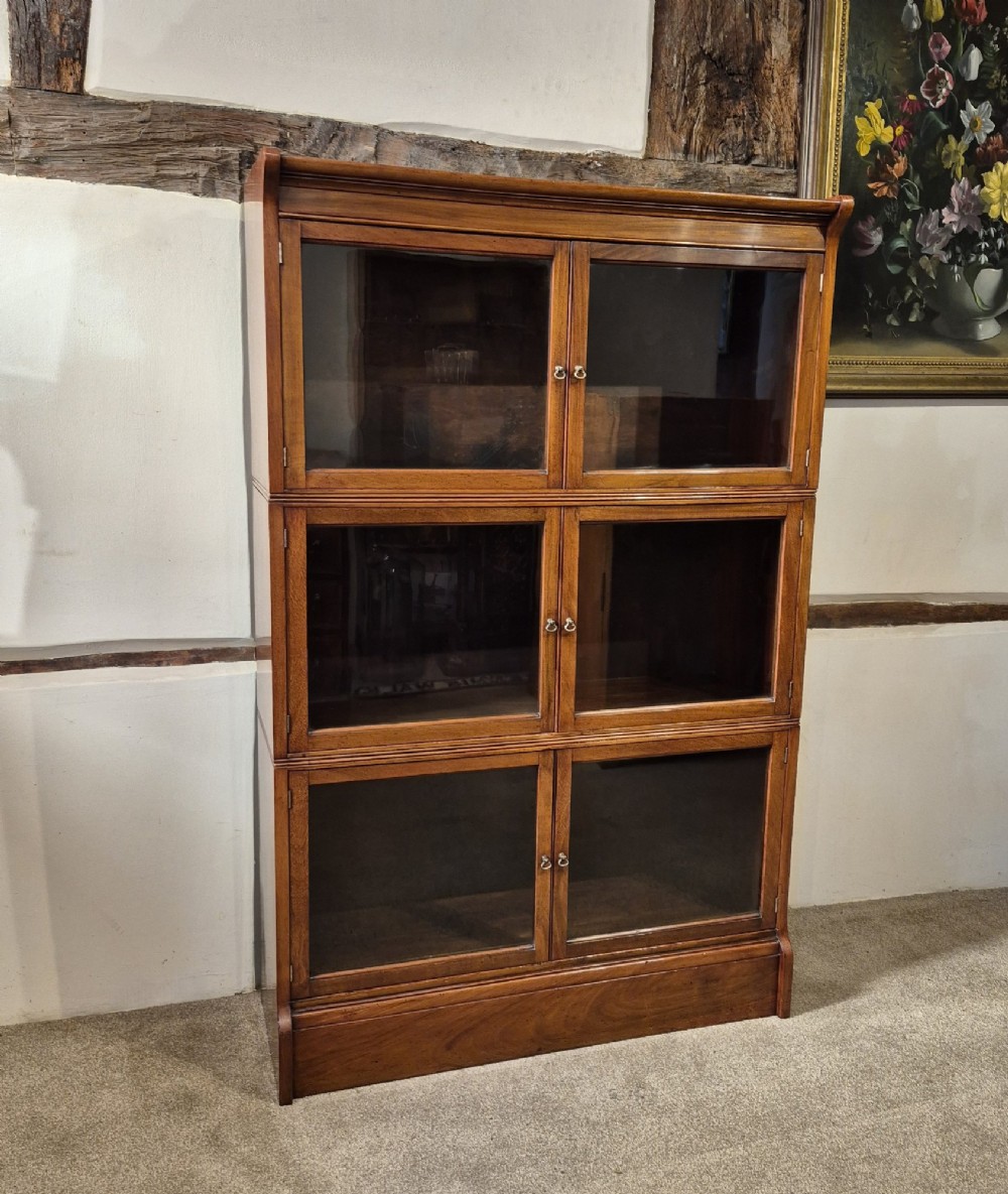 A three-tier warm brown oak sectional bookcase with double glazed doors and brass ring handles.