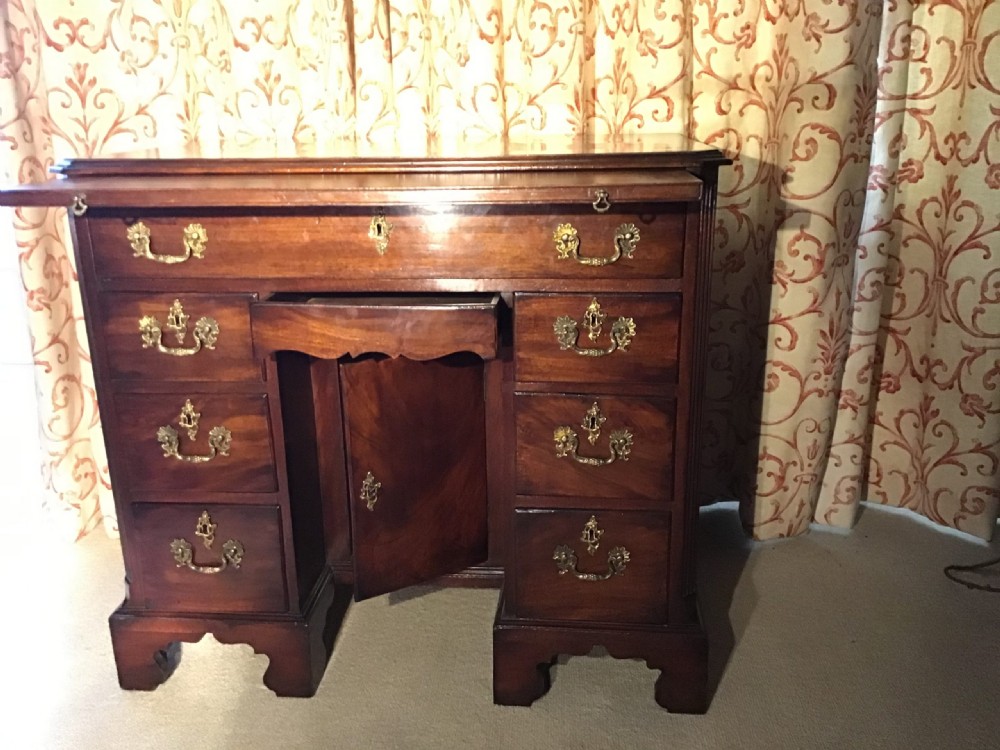 An 18th-century George III mahogany kneehole desk featuring a long top drawer over six side drawers, a central recessed cupboard, brass handles, and bracket feet. View X