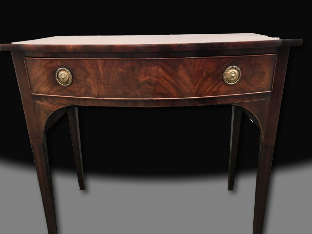 A late 18th-century George III mahogany bow front side table featuring a central drawer with circular brass handles and slender tapered legs. View II